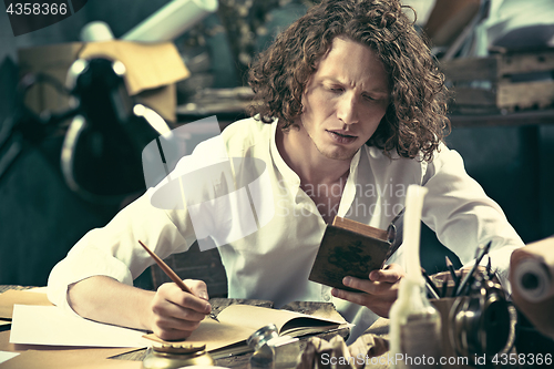 Image of Writer at work. Handsome young writer sitting at the table and writing something in his sketchpad