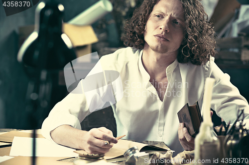 Image of Writer at work. Handsome young writer sitting at the table and writing something in his sketchpad