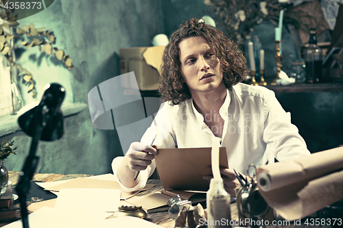 Image of Writer at work. Handsome young writer sitting at the table and writing something in his sketchpad