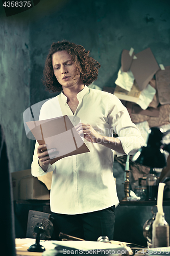 Image of Writer at work. Handsome young writer standing near the table and making up something in his mind