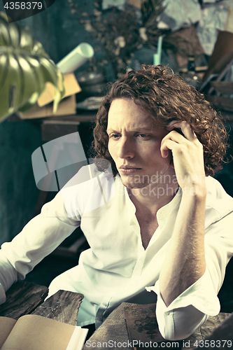 Image of Writer at work. Handsome young writer sitting at the table and writing something in his sketchpad