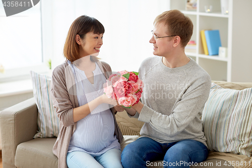 Image of happy husband giving flowers to his pregnant wife