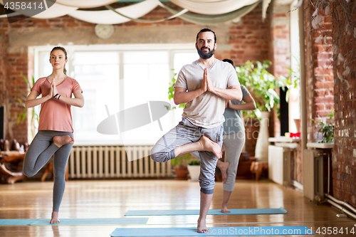 Image of group of people doing yoga tree pose at studio