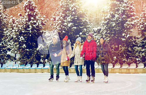 Image of happy friends ice skating on rink outdoors