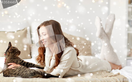 Image of happy young woman with cat lying in bed at home