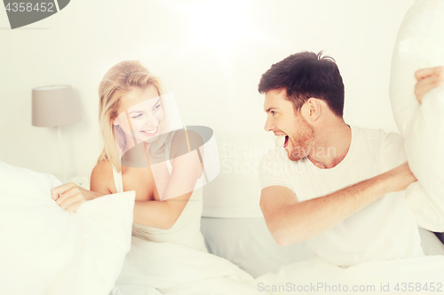 Image of happy couple having pillow fight in bed at home