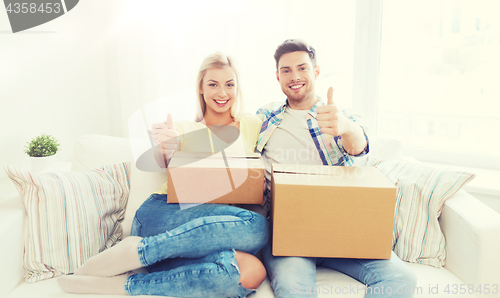 Image of happy couple with boxes showing thumbs up at home