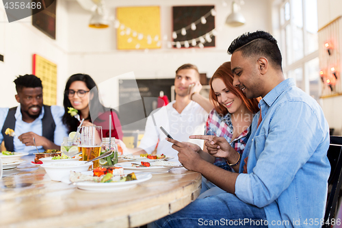 Image of happy friends with smartphones at restaurant