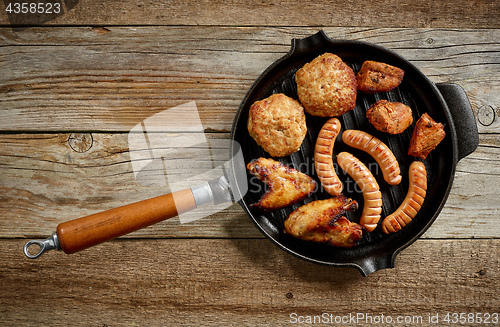 Image of various grilled meat and fried potatoes on cast iron pan
