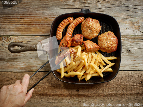 Image of various grilled meat and fried potatoes on cast iron pan