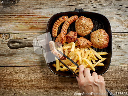 Image of meat sausages and fried potatoes on cast iron pan