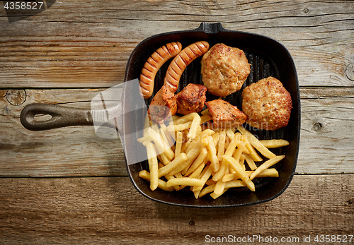 Image of various grilled meat and fried potatoes on cast iron pan