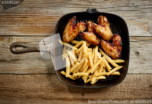 Image of chicken wings and fried potatoes on cast iron pan