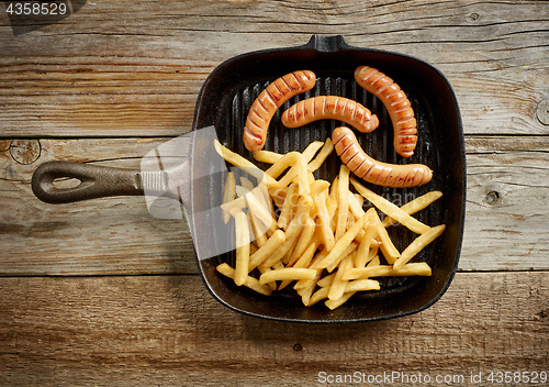 Image of meat sausages and fried potatoes on cast iron pan