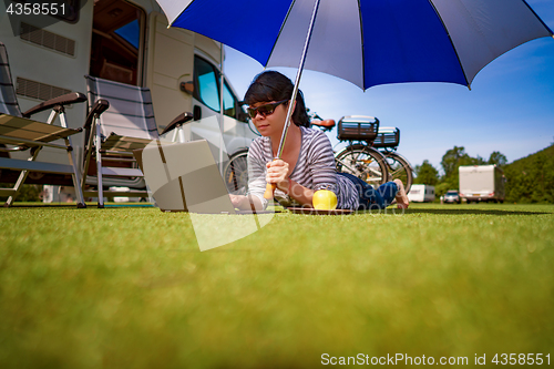 Image of Woman on the grass, looking at the laptop under umbrella near th