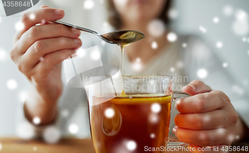 Image of close up of woman adding honey to tea with lemon