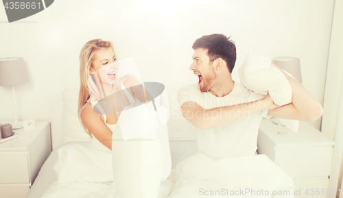 Image of happy couple having pillow fight in bed at home