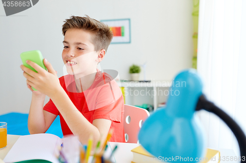 Image of student boy with smartphone distracting from study