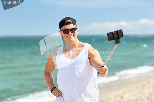 Image of man with smartphone selfie stick on summer beach