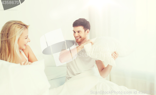 Image of happy couple having pillow fight in bed at home