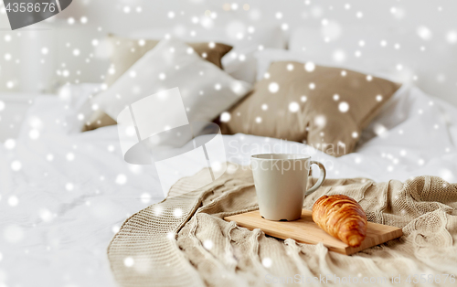 Image of coffee cup and croissant on plaid in bed at home