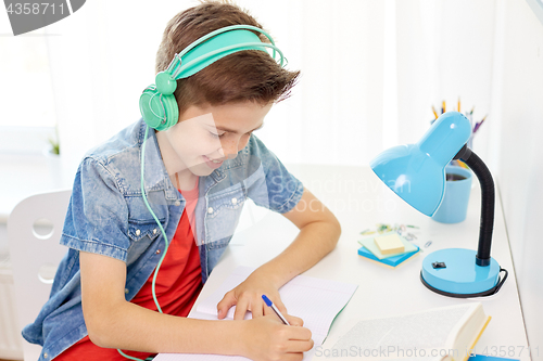 Image of student boy in headphones writing to notebook
