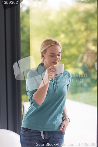 Image of young woman drinking morning coffee by the window