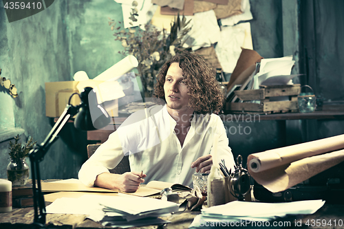 Image of Writer at work. Handsome young writer sitting at the table and writing something in his sketchpad