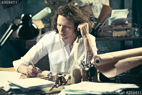 Image of Writer at work. Handsome young writer sitting at the table and writing something in his sketchpad