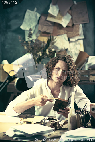 Image of Writer at work. Handsome young writer sitting at the table and writing something in his sketchpad