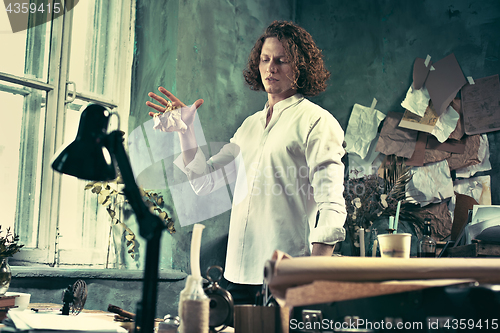 Image of Writer at work. Handsome young writer standing near the table and making up something in his mind