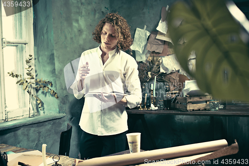 Image of Writer at work. Handsome young writer standing near the table and making up something in his mind