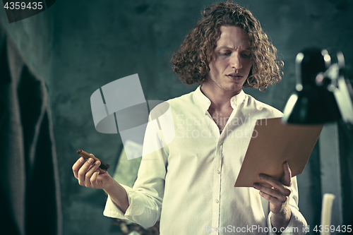 Image of Writer at work. Handsome young writer standing near the table and making up something in his mind