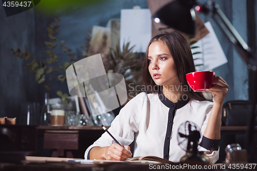 Image of Young beautiful woman working with cup of coffee