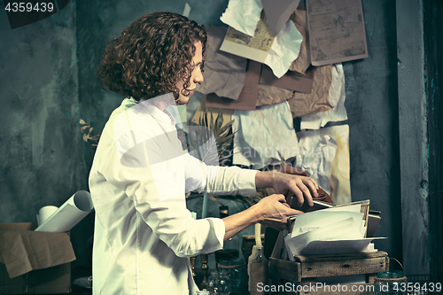 Image of Writer at work. Handsome young writer standing near the table and making up something in his mind