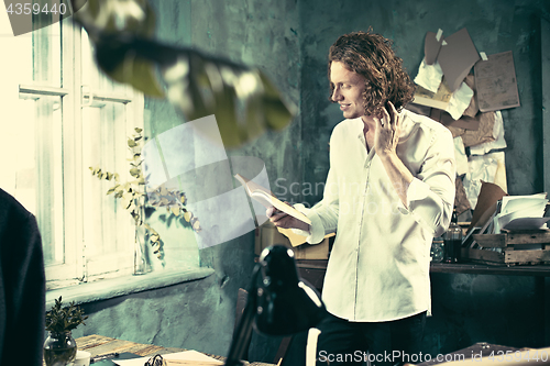 Image of Writer at work. Handsome young writer standing near the table and making up something in his mind