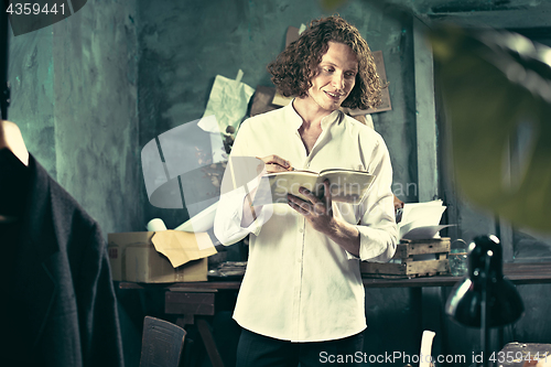 Image of Writer at work. Handsome young writer standing near the table and making up something in his mind