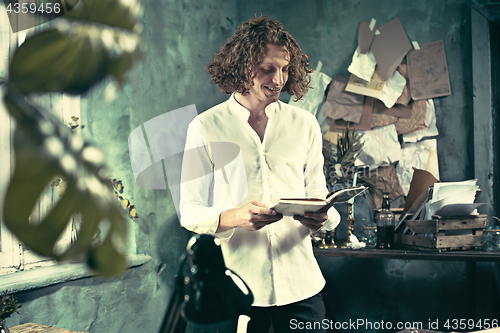 Image of Writer at work. Handsome young writer standing near the table and making up something in his mind