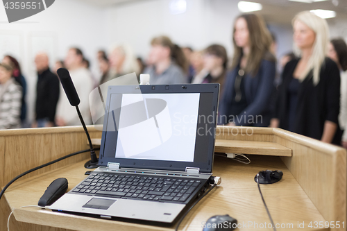 Image of Laptop and microphone on the rostrum in lecture hall full of conference participants.