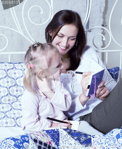 Image of portrait of mother and daughter laying in bed reading and writing, lifestyle people concept
