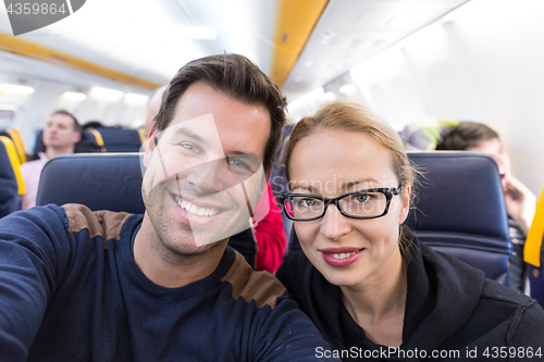 Image of Young handsome couple taking a selfie on commercial airplane.