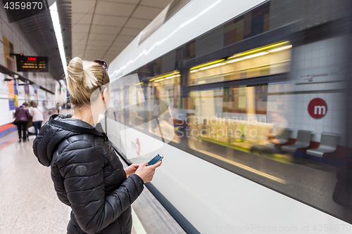 Image of Woman with a cell phone waiting for metro.