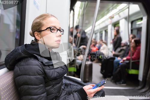 Image of Young girl with mobile phone traveling on metro.