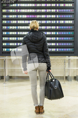 Image of Female traveller checking a departures board at the airport terminal hall.