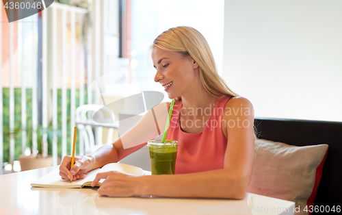 Image of woman with drink writing to notebook at restaurant