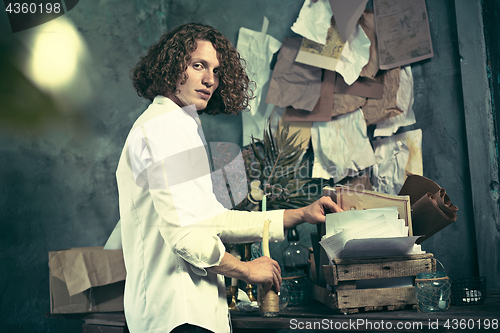 Image of Writer at work. Handsome young writer standing near the table and making up something in his mind