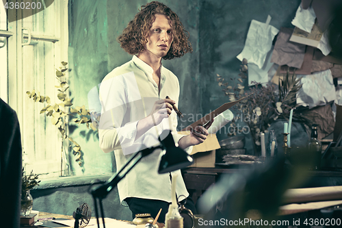 Image of Writer at work. Handsome young writer standing near the table and making up something in his mind