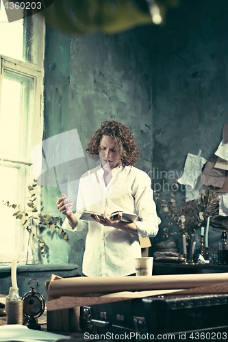 Image of Writer at work. Handsome young writer standing near the table and making up something in his mind