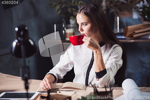 Image of Young beautiful woman working with cup of coffee