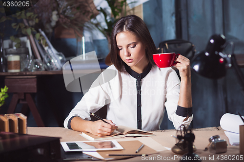 Image of Young beautiful woman working with cup of coffee